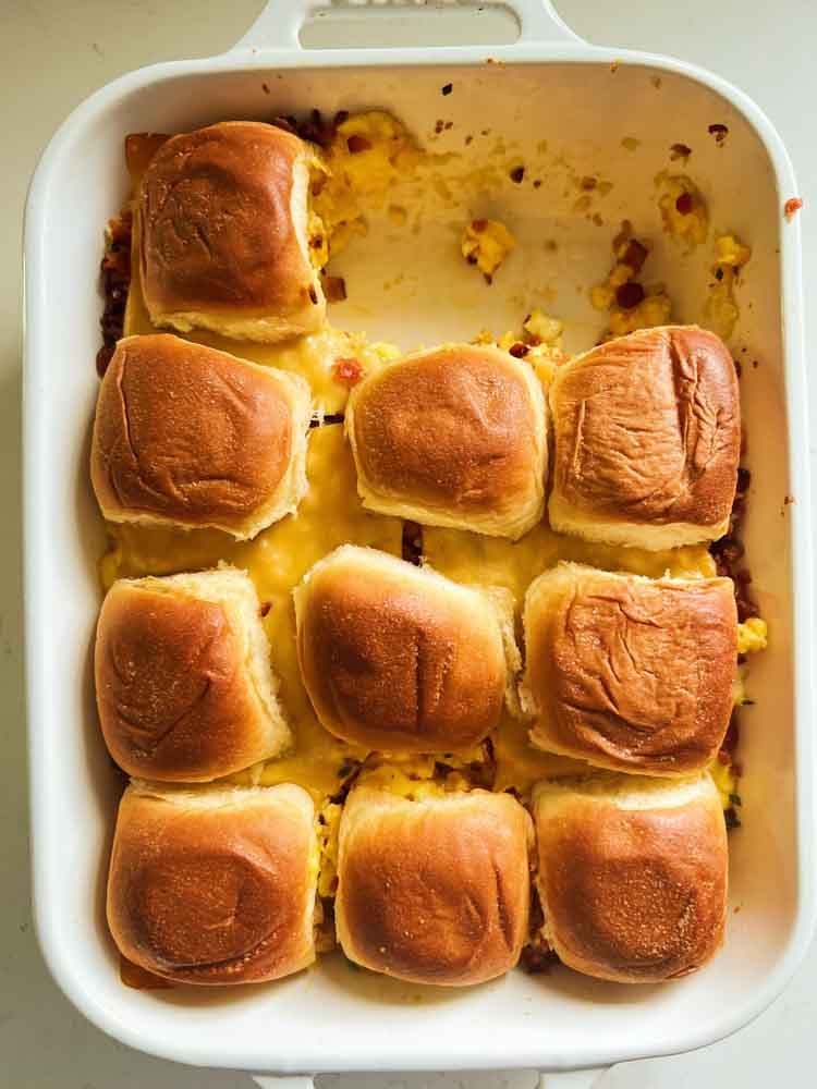 a baking dish filled with hawaiian roll breakfast sliders - two of them are missing. 