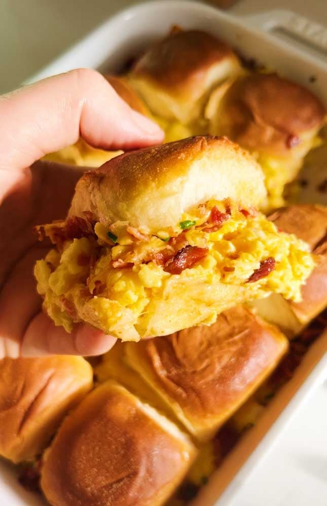 a hand holding a hawaiian roll breakfast sandwich