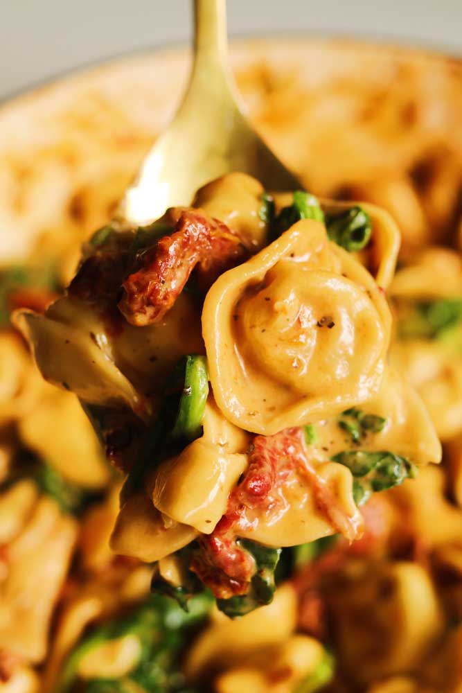 a fork holding a few tortellini in a creamy sun dried tomato spinach sauce. 