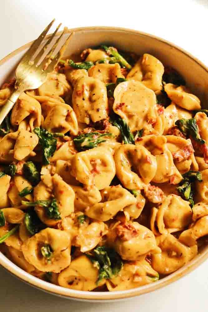 a white bowl filled with creamy tortellini in a spinch and sun dried tomato cream sauce. 