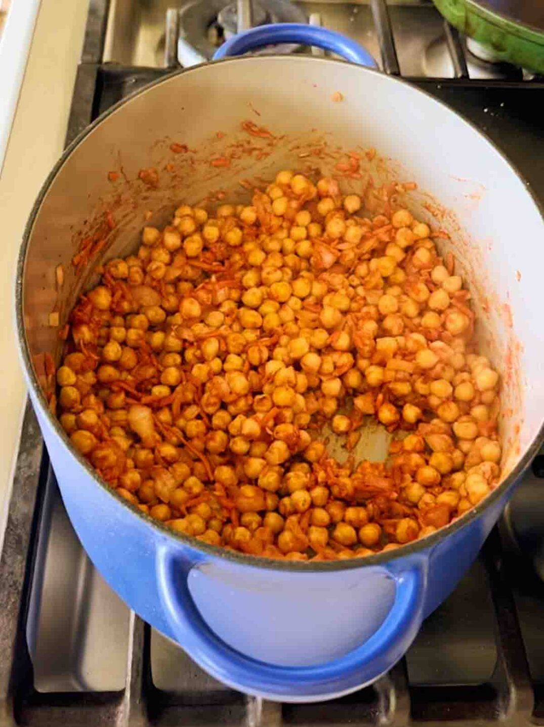 chickpeas tossed in tomato paste in a big blue pot.