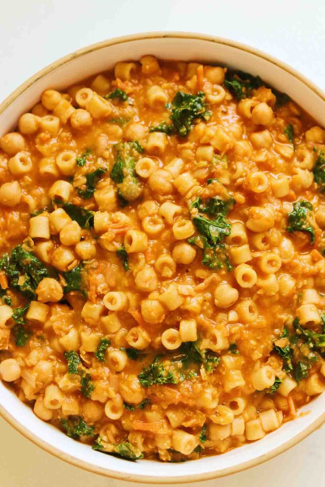 chickpeas, pasta, kale and parmesan broth in a white bowl. 