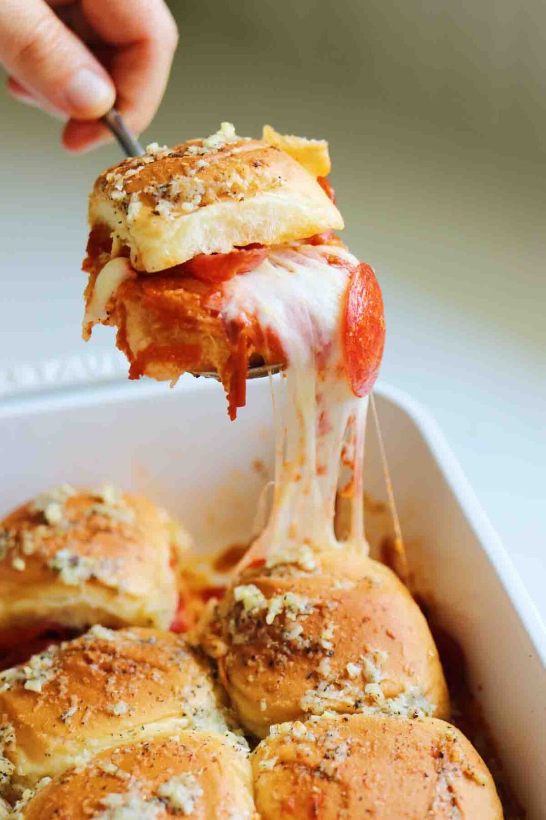a pizza slider being pulled out of the baking dish with drippy gooey cheese.