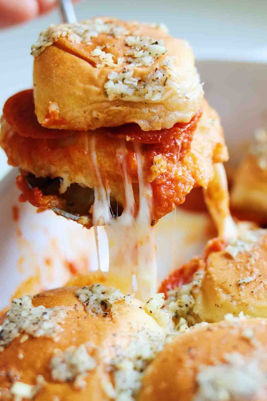 a pizza sliders with a mozzarella cheese pull being stretched from the pan to the fork.