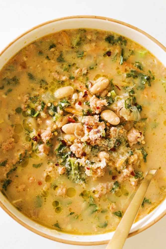 a white bowl filled with creamy sausage, kale, and white bean soup. 