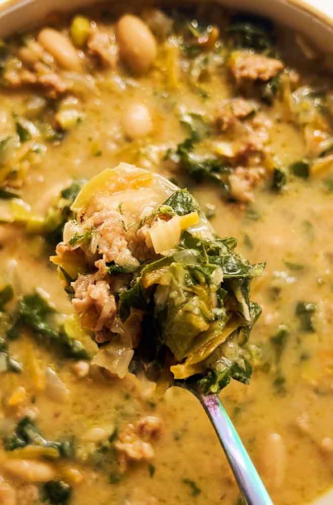 a spoon holding a bit of sausage, kale, and white bean soup. 