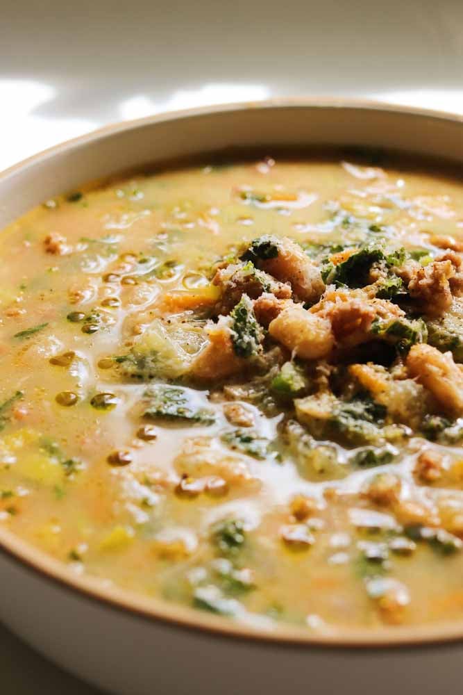 the left side of a white bowl filled with sausage, kale, and white bean soup. 