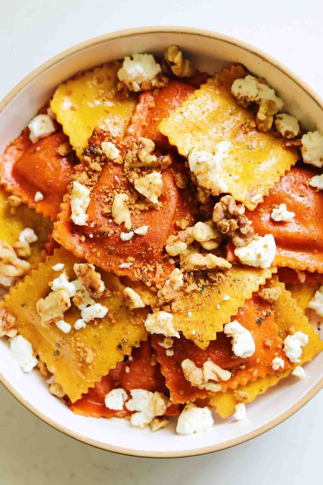 Trader Joe's colorful pumpkin ravioli in a white bowl topped with goat cheese.