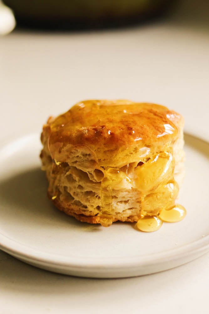 a honey butter biscuit drizzled with lots of golden honey on a white plate. 