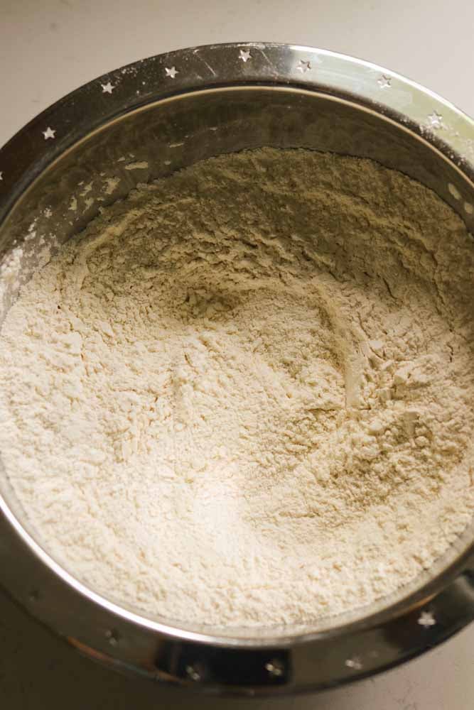 a silver mixing bowl full of flour, baking powder, sugar and salt. 