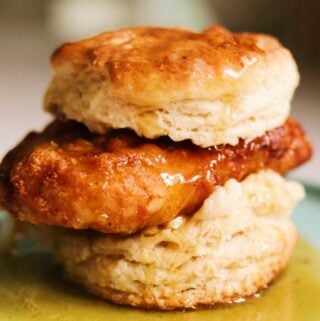 a honey butter fried chicken biscuit sitting on a blue plate.