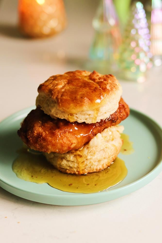 a blue plate with a honey butter chicken biscuit dripping with honey.