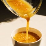 a glass jar pouring out maple dijon dressing.