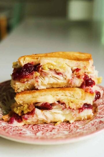 two halves of a turkey cranberry sandwich sitting on top of each other on a pink and white plate.
