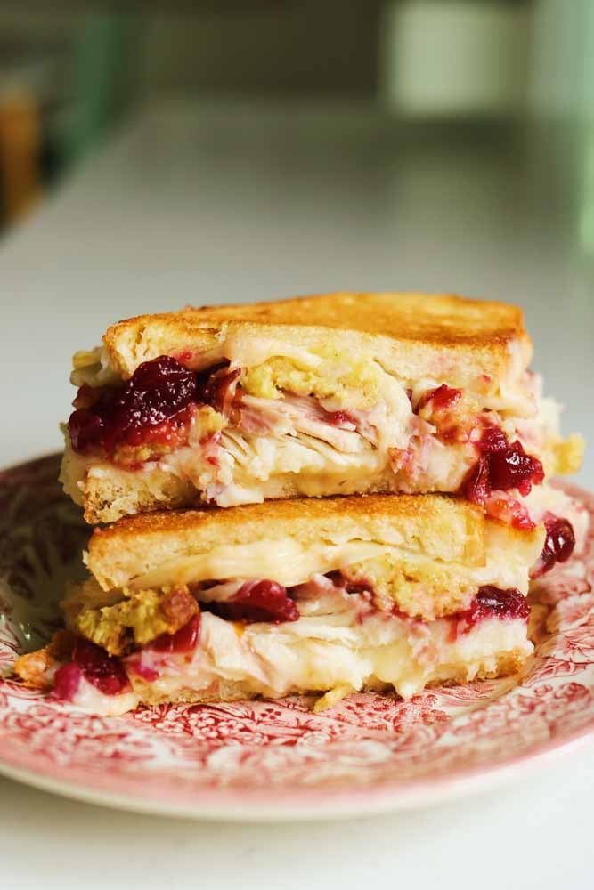 two halves of a turkey cranberry sandwich sitting on top of each other on a pink and white plate. 