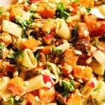 a white bowl filled with butternut squash, kale, apple, candied nuts and pasta for winter pasta salad recipe.
