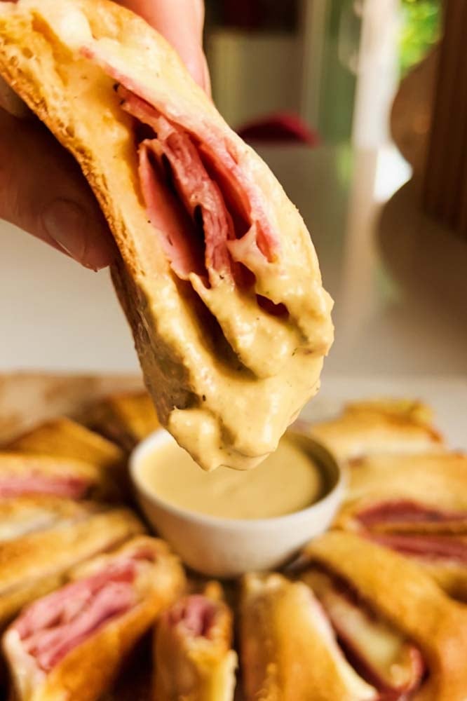 a hand dipping a piece of italian grinder crescent roll ring into sauce. 