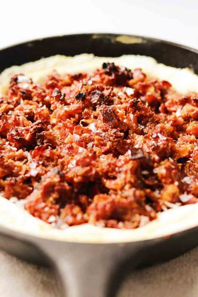 whipped cheese topped with candied bacon and dates in a black cast iron skillet