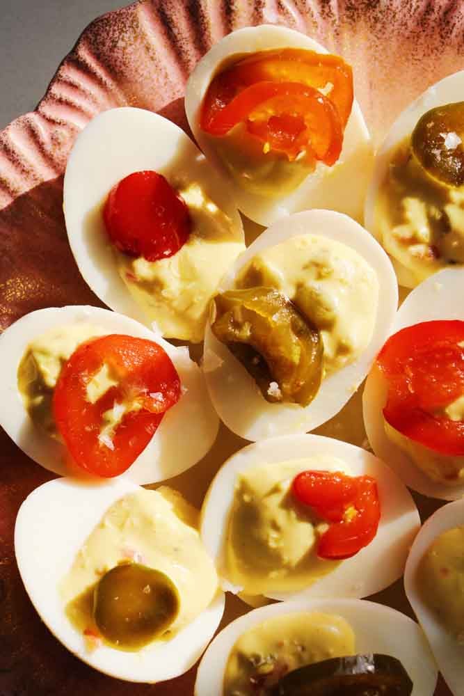 the top left side of a pink and gold plate filled with colorful candied jalapeno deviled eggs.