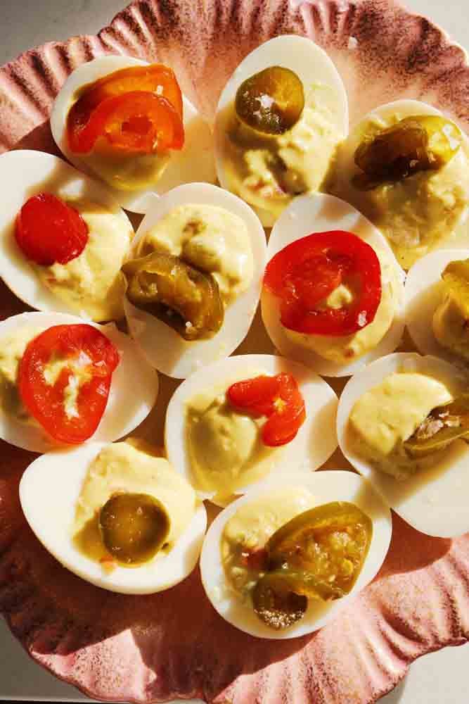 12 candied jalapeno deviled eggs on a pink scalloped plate. 