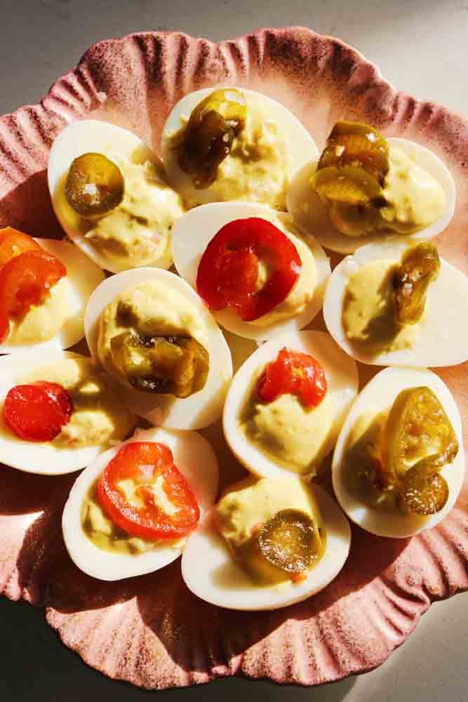a pink and gold plate filled with red and green topped candied jalapeno deviled eggs. 