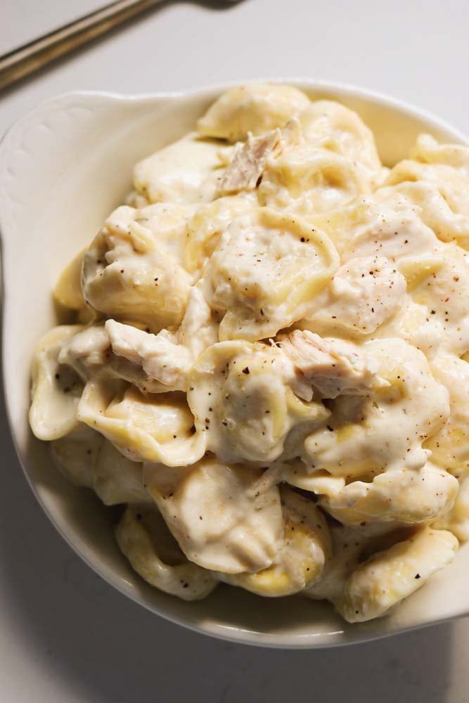 a white bowl filled with a serving of chicken tortellini alfredo. 