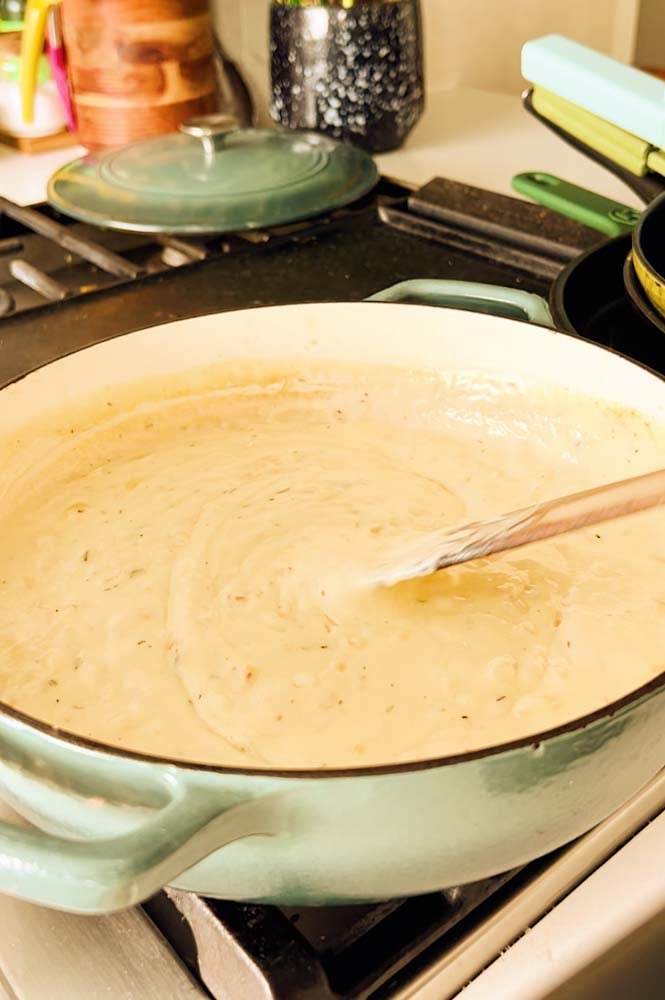 a cheesy gruyere sauce being made in a blue braising pot.