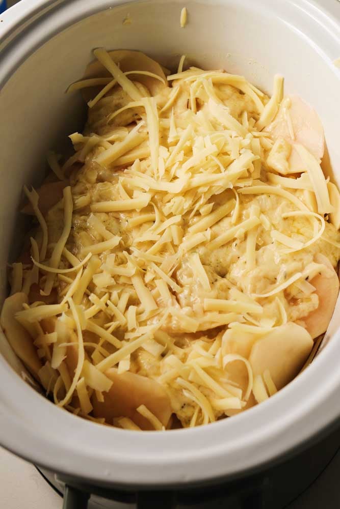 a green crockpot being filled with layers of crockpot potatoes au gratin. 