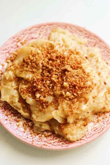 Cheesy crockpot potatoes au gratin on a pink and white antique plate.