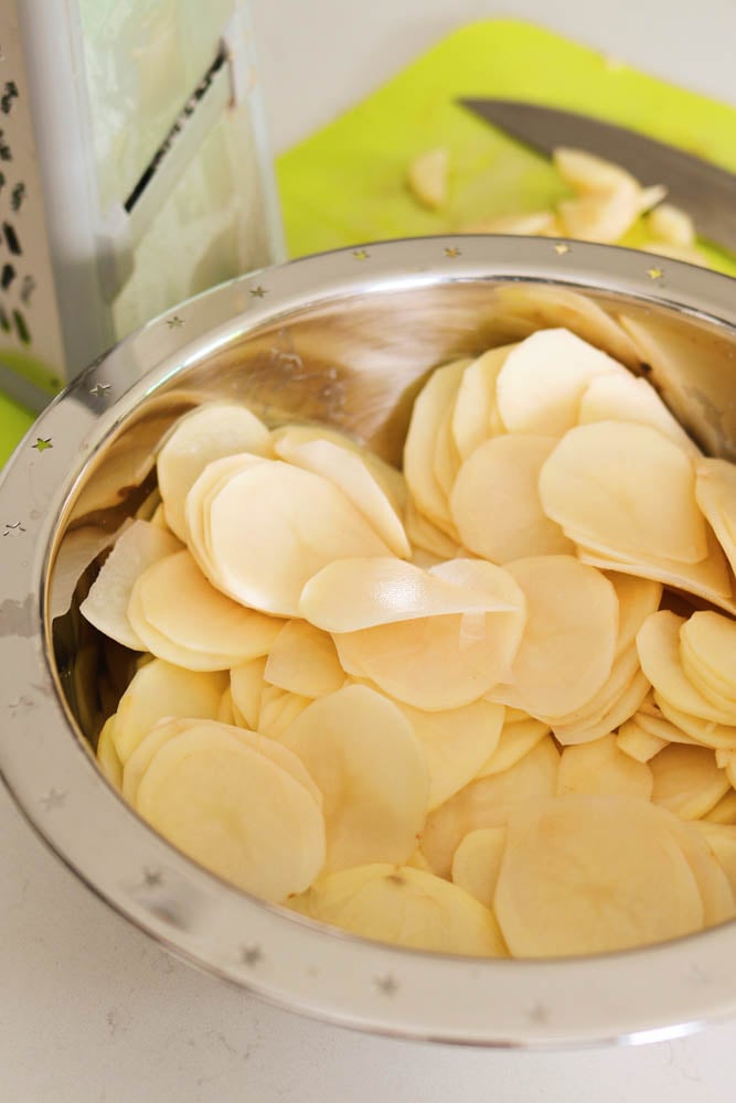 thinly sliced potatoes in a silver bowl.