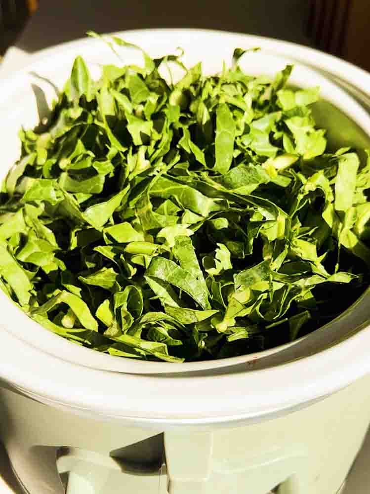 raw chopped collard greens in a green crockpot.