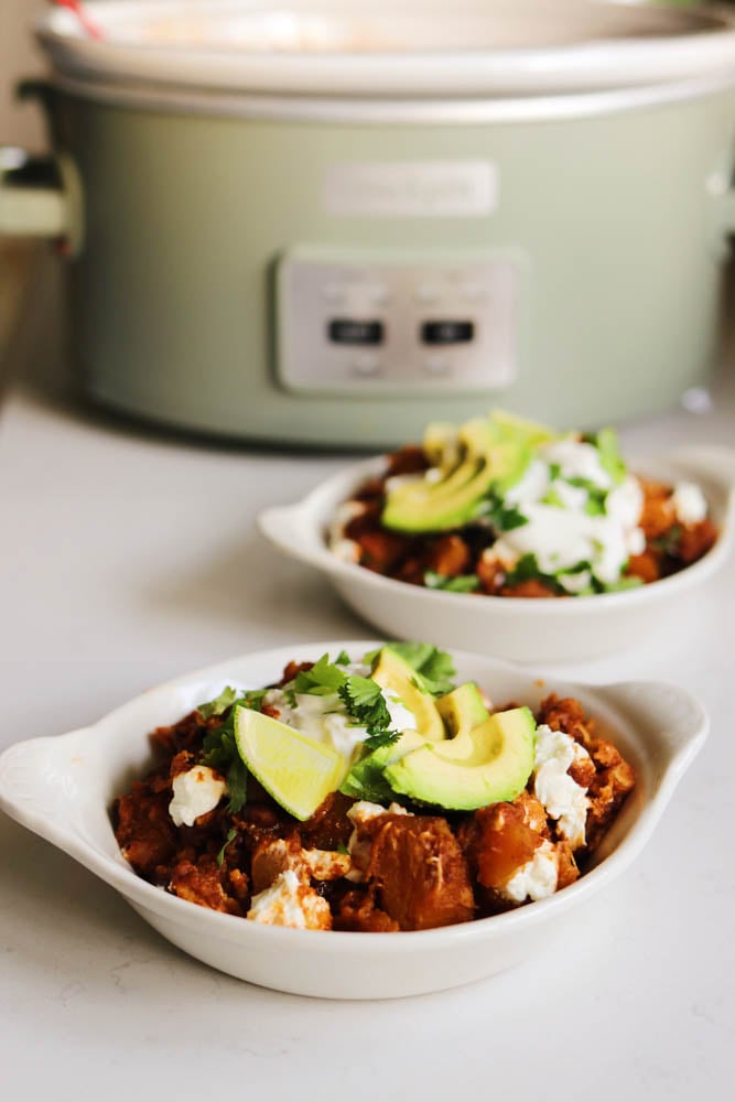 a green crockpot with two bowls of crockpot enchilada casserole in front of it. 