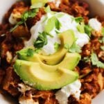 a bowl of crockpot enchilada casserole made with butternut squash and goat cheese with avocado and sour cream on top.