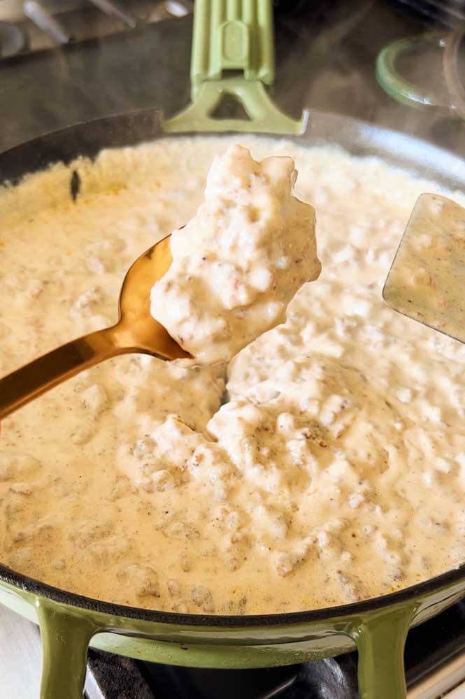 Sausage Gravy in a skillet with a spoon showing the thick consistency. 