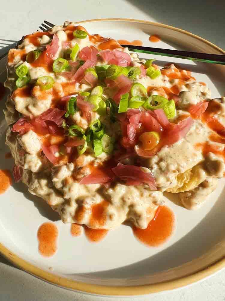 A big plate of Sausage Gravy and Biscuits with pickled red onions, scallions and hot sauce on top.