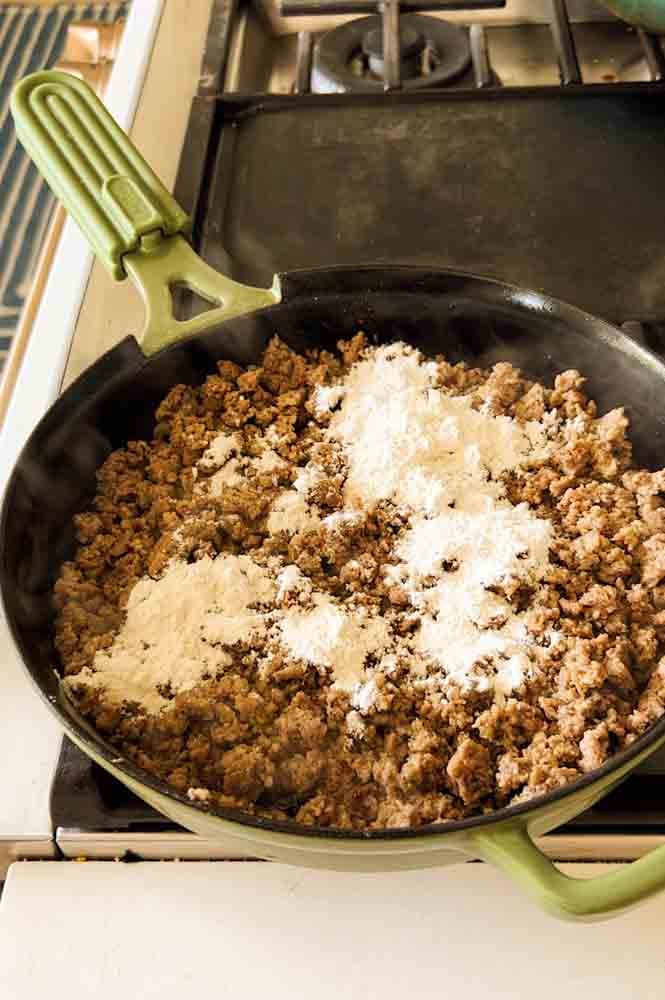 sausage crumbles in a cast iron skillet with flour on top. 