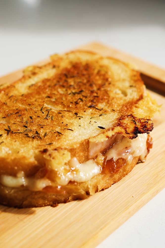 a gruyere grilled cheese sitting on a cutting board with cheese oozing out. 