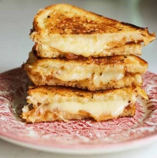 a gruyere grilled cheese sitting on a pink plate with cheese oozing out.
