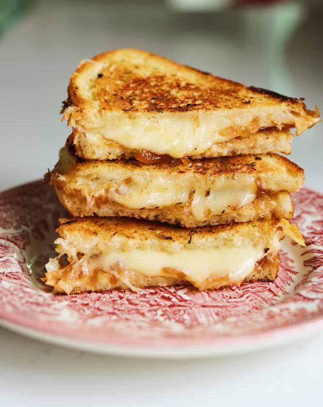 a gruyere grilled cheese sitting on a pink plate with cheese oozing out.