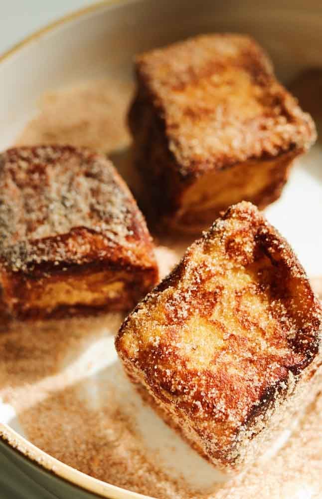 a bowl of cinnamon sugar with pieces of hawaiian roll french toast in it. 