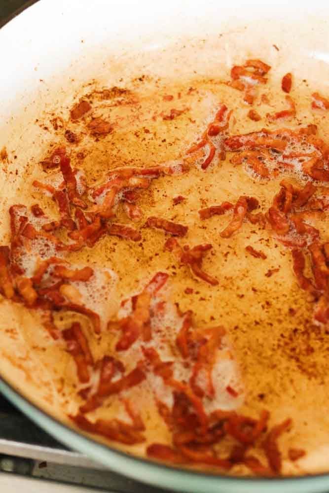 tiny bits of bacon frying in a blue braising pot. 