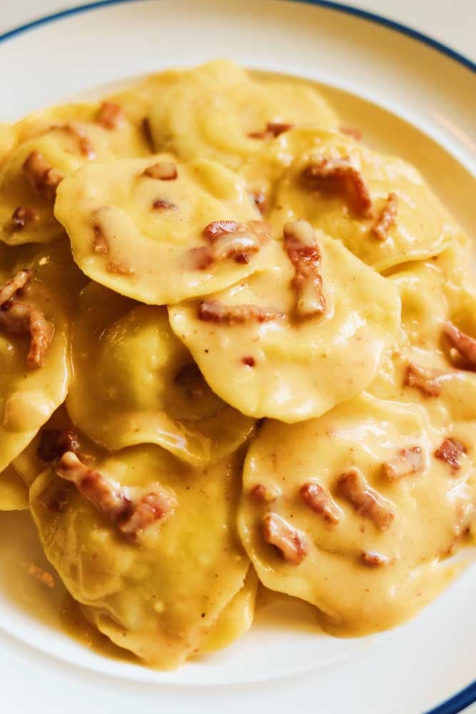 ravioli carbonara on a white plate with a blue rim. 