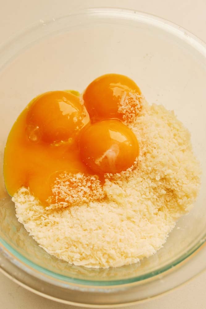 egg yolks and parmigiano cheese in a clear bowl. 