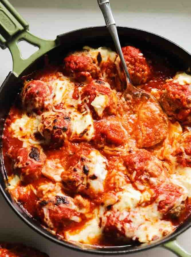 ricotta meatballs swimming in red sauce in a green cast iron skillet.