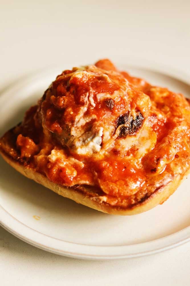 a ricotta meatball with sauce on top of a piece of toasted ciabatta bread.