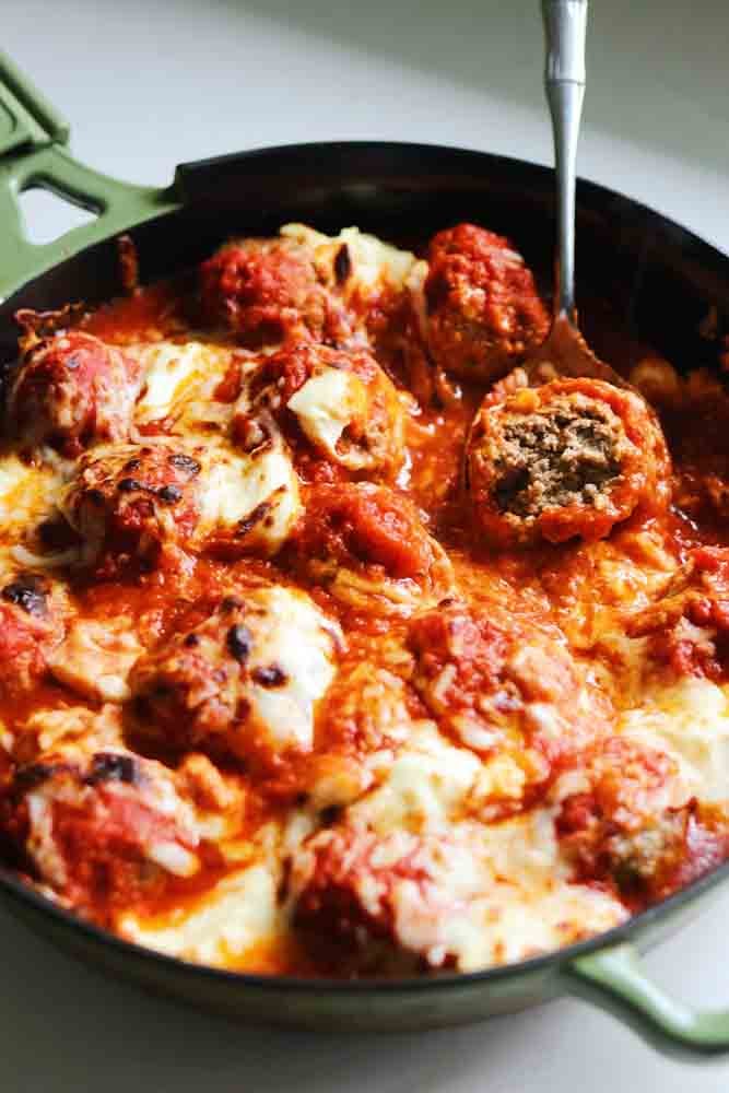 a cast iron skillet filled with ricotta meatballs, marinara sauce and melted cheese.