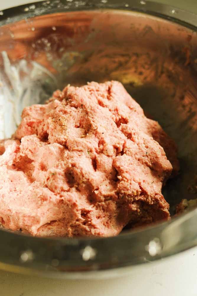 raw ground beef in a silver bowl with seasoning and ricotta cheese.