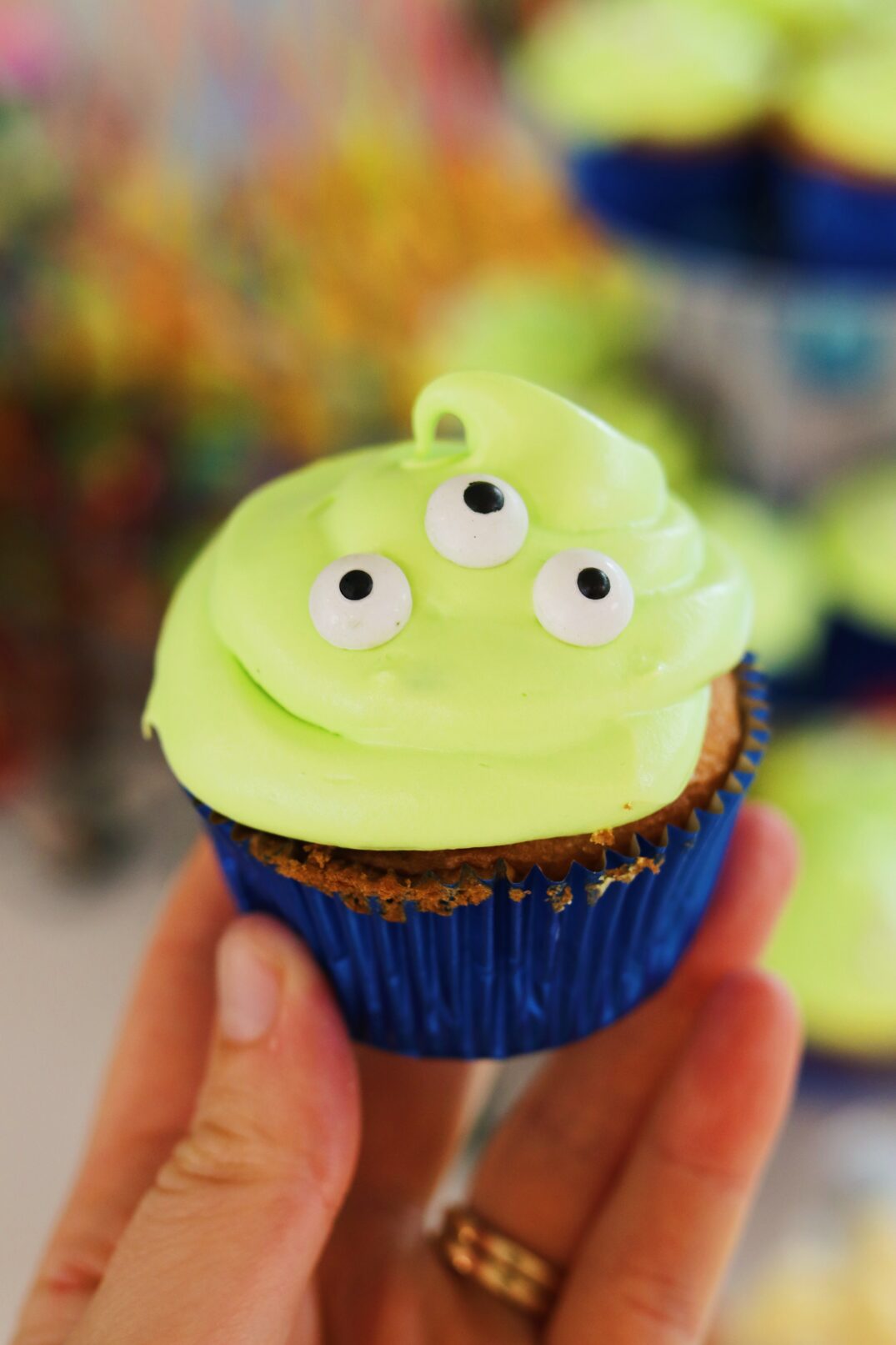 a hand holding a homemade toy story alien cupcake. 