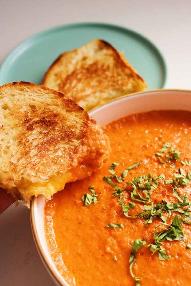 a bowl of creamy tomato soup with a grilled cheese on the side. 