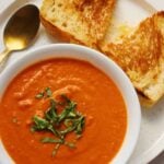 grilled cheese and tomato soup on a white plate with a white bowl and a golden spoon.